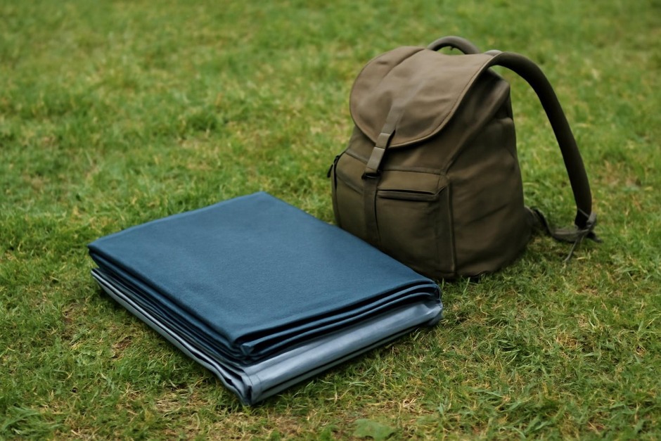 A neatly folded homemade groundsheet on grass next to a backpack